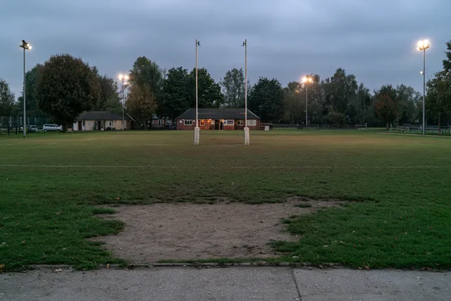 Terrain d’un club de rugby local au crépuscule, poteaux en H et petit club-house en arrière-plan